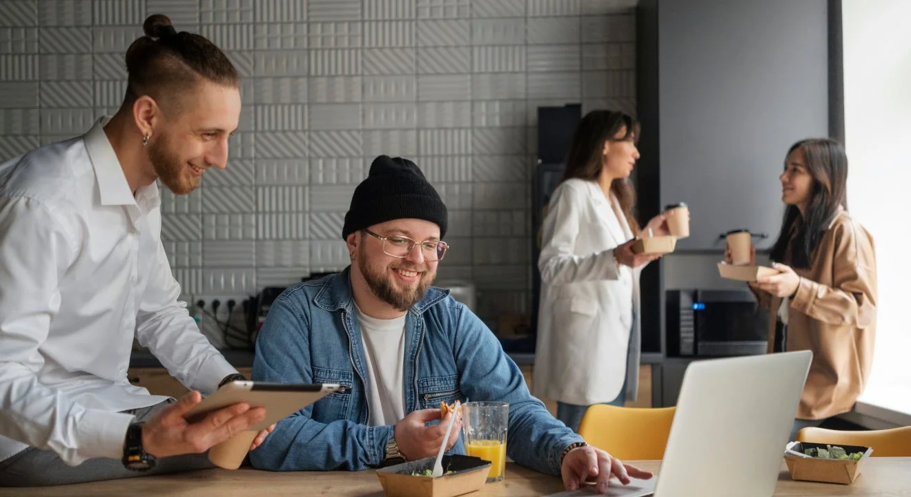 Two colleagues laughing over a tablet at a shared office table