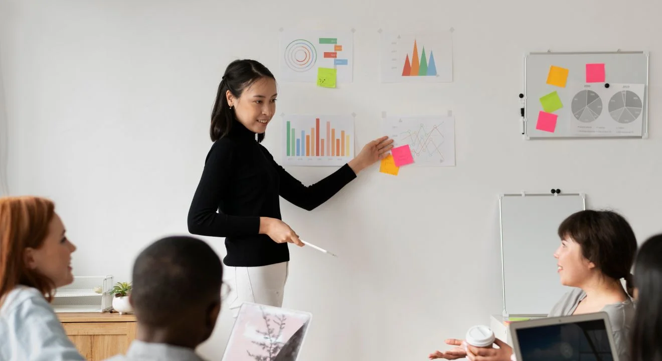 A speaker presenting charts and sticky notes to a seated meeting room