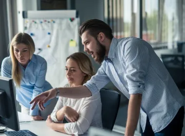 Three colleagues gathered around a monitor, one pointing at the screen