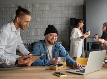 Two colleagues laughing over a tablet at a shared office table