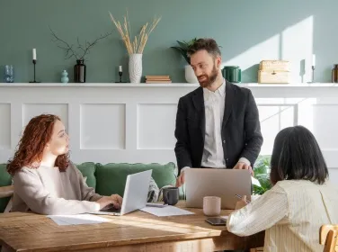 Three people working on laptops around a table in a bright green room