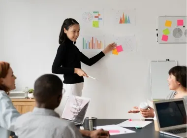 A speaker presenting charts and sticky notes to a seated meeting room