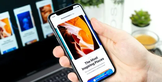 A hand holding a phone showing an article screen in front of a laptop