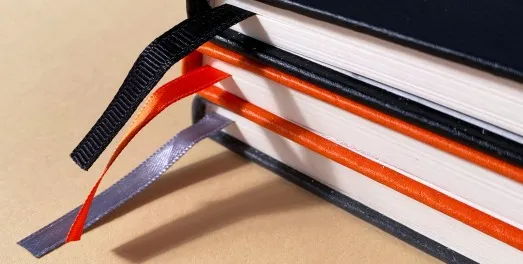 A close-up of a hardback book edge with black, orange and grey ribbon markers