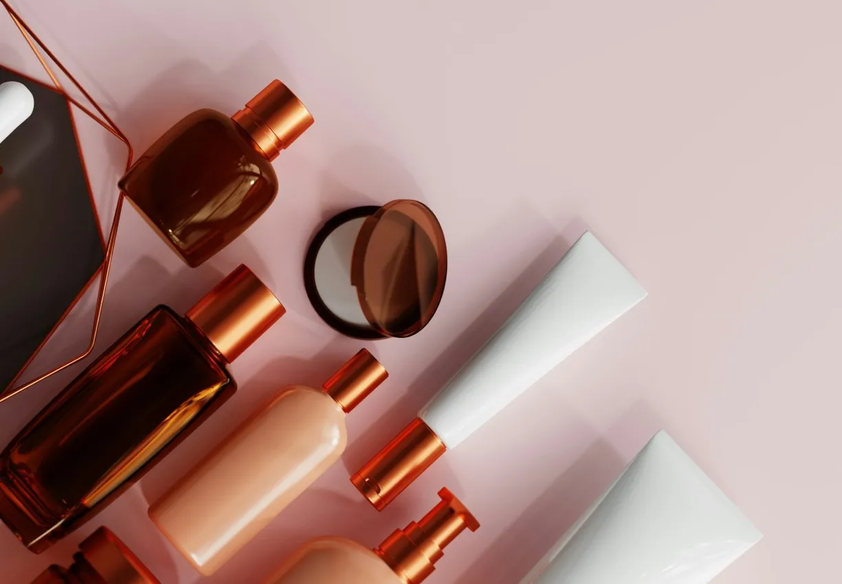Copper and amber cosmetics bottles, tubes and a compact arranged on a soft pink background