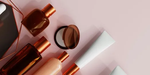 Copper-toned cosmetics bottles and tubes arranged on a pink background