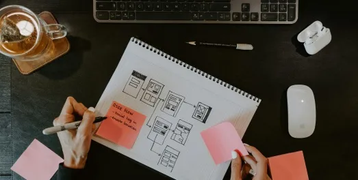 Hands sketching a user flow on grid paper beside a keyboard and mouse